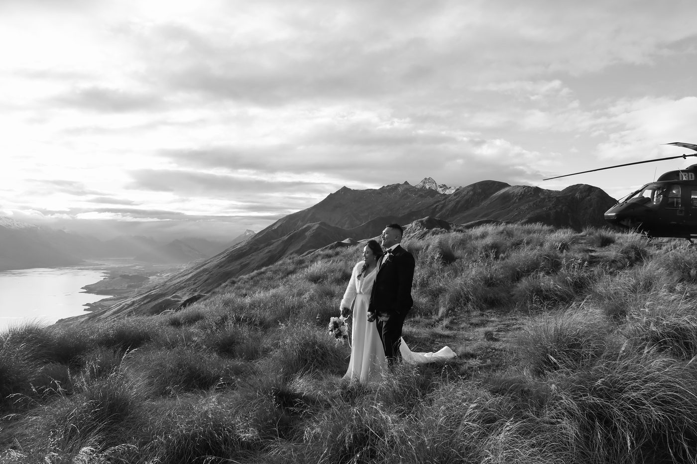 Couple eloping on a Queenstown mountain ridge, helicopter waiting behind them